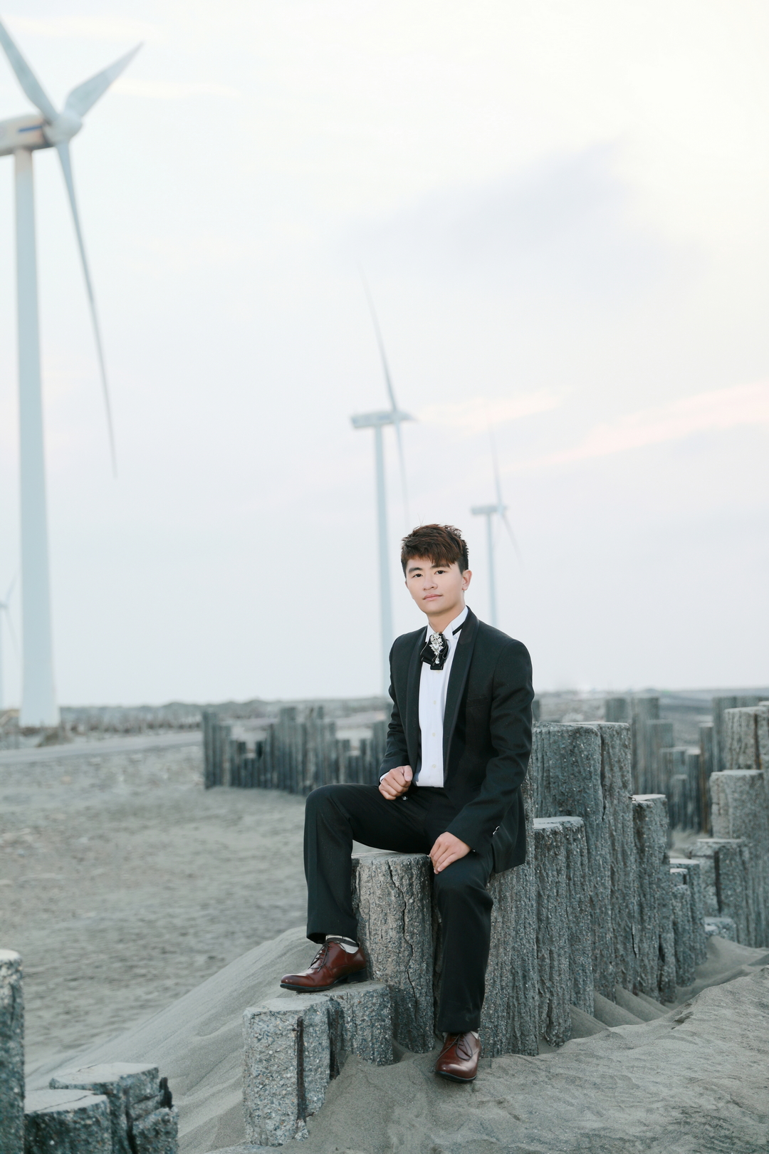 黑西服坐姿構圖於風車沙地